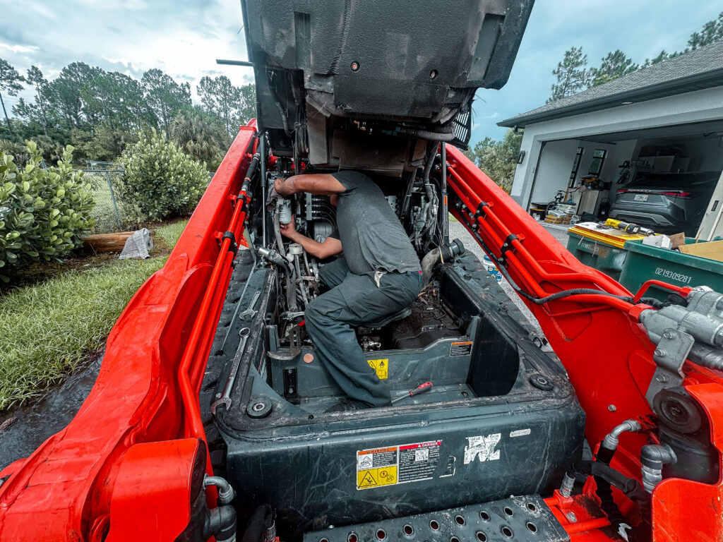 Technician performing maintenance on hydraulic system of askid steer at equipment rental service.